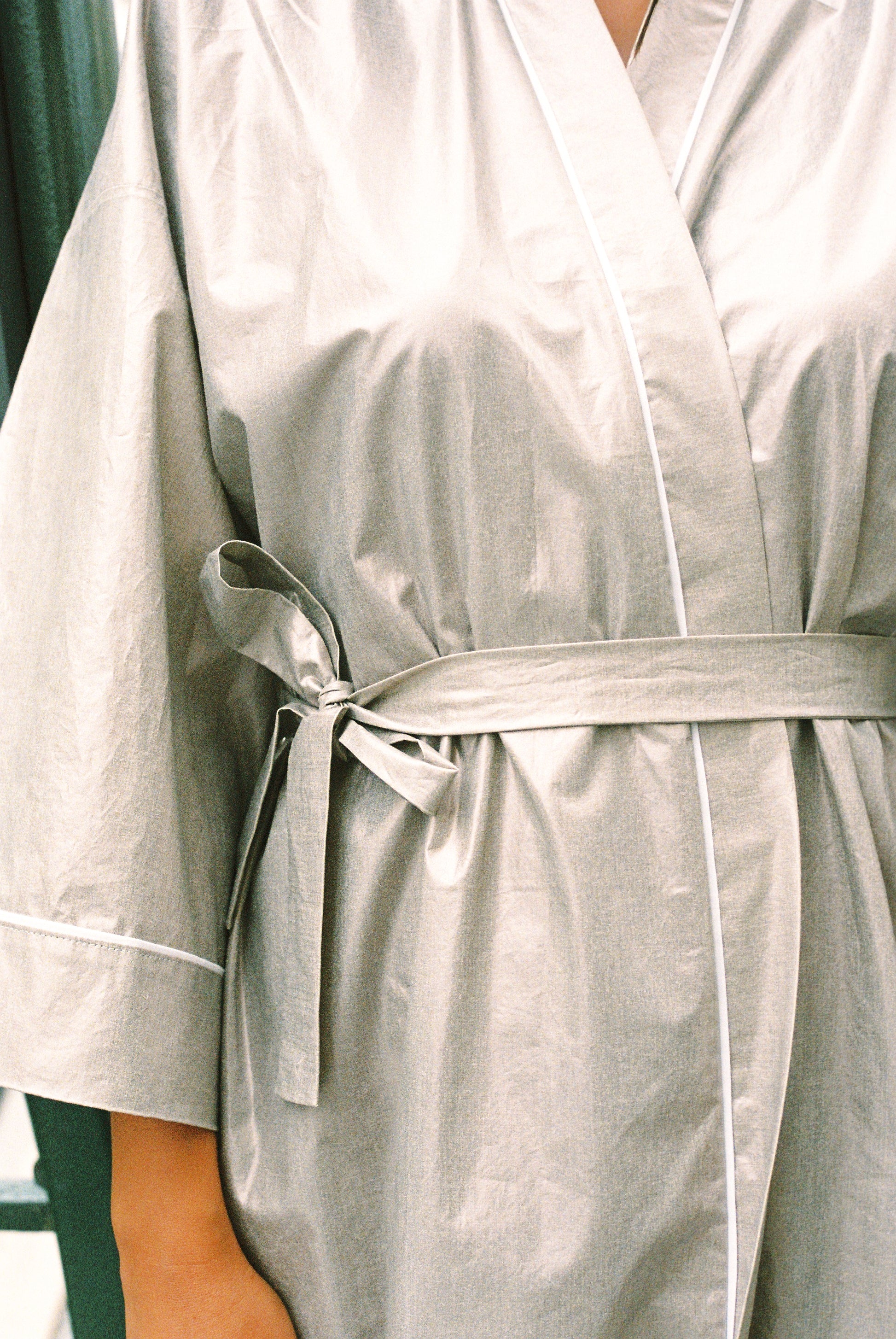 Atelier Sarita – Kimono Crystal en popeline de coton argenté. Long kimono fluide à la coupe affirmée, ceinturé à la taille, confectionné à la main à Paris en série limitée. Une pièce audacieuse et urbaine, inspirée des reflets minéraux et des lumières de l’architecture parisienne.