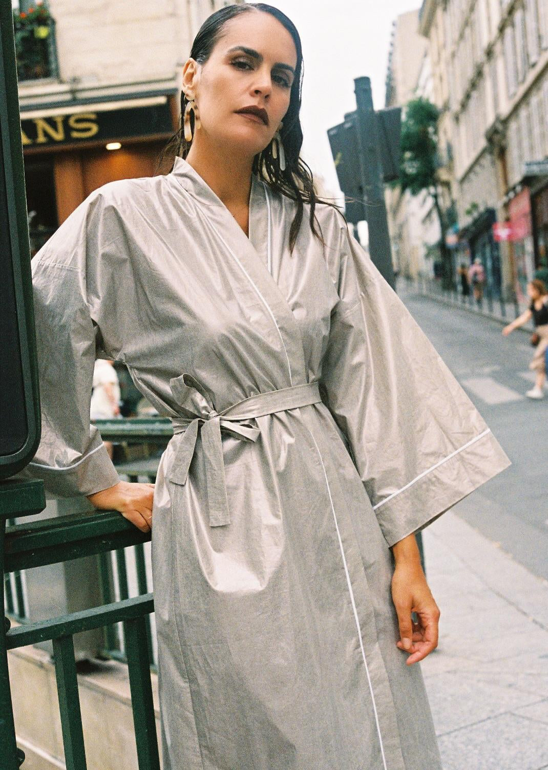 Atelier Sarita – Kimono Crystal en popeline de coton argenté. Long kimono fluide à la coupe affirmée, ceinturé à la taille, confectionné à la main à Paris en série limitée. Une pièce audacieuse et urbaine, inspirée des reflets minéraux et des lumières de l’architecture parisienne.