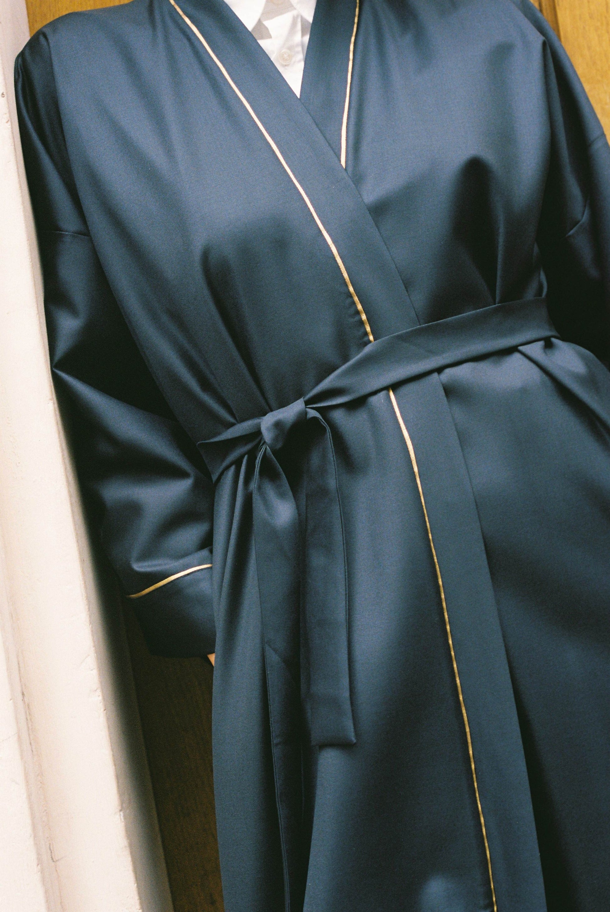 Atelier Sarita – Kimono Garnier en laine de costume bleu marine, rehaussé de délicats passepoils en soie dorée. Une coupe longue et fluide, inspirée de l’élégance intemporelle de l’Opéra Garnier, qui incarne la grandeur et la finesse de l’architecture parisienne. Fabriqué à la main à Paris en série très limitée, ce kimono allie la profondeur classique du bleu marine à la lumière subtile de l’or, pour une silhouette sophistiquée et affirmée.