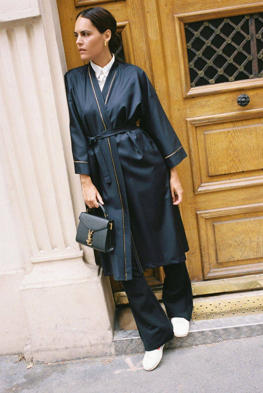 Atelier Sarita – Kimono Garnier en laine de costume bleu marine, rehaussé de délicats passepoils en soie dorée. Une coupe longue et fluide, inspirée de l’élégance intemporelle de l’Opéra Garnier, qui incarne la grandeur et la finesse de l’architecture parisienne. Fabriqué à la main à Paris en série très limitée, ce kimono allie la profondeur classique du bleu marine à la lumière subtile de l’or, pour une silhouette sophistiquée et affirmée.