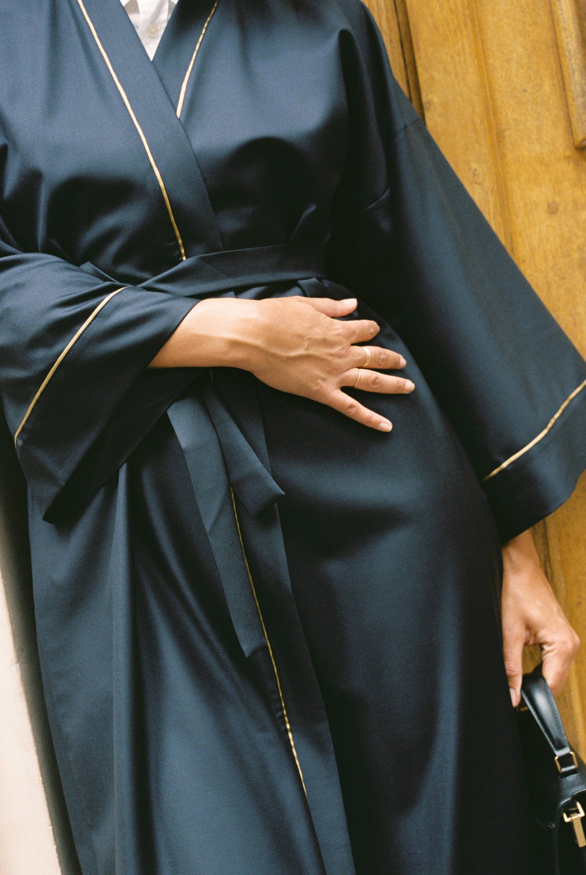 Atelier Sarita – Kimono Garnier en laine de costume bleu marine, rehaussé de délicats passepoils en soie dorée. Une coupe longue et fluide, inspirée de l’élégance intemporelle de l’Opéra Garnier, qui incarne la grandeur et la finesse de l’architecture parisienne. Fabriqué à la main à Paris en série très limitée, ce kimono allie la profondeur classique du bleu marine à la lumière subtile de l’or, pour une silhouette sophistiquée et affirmée.