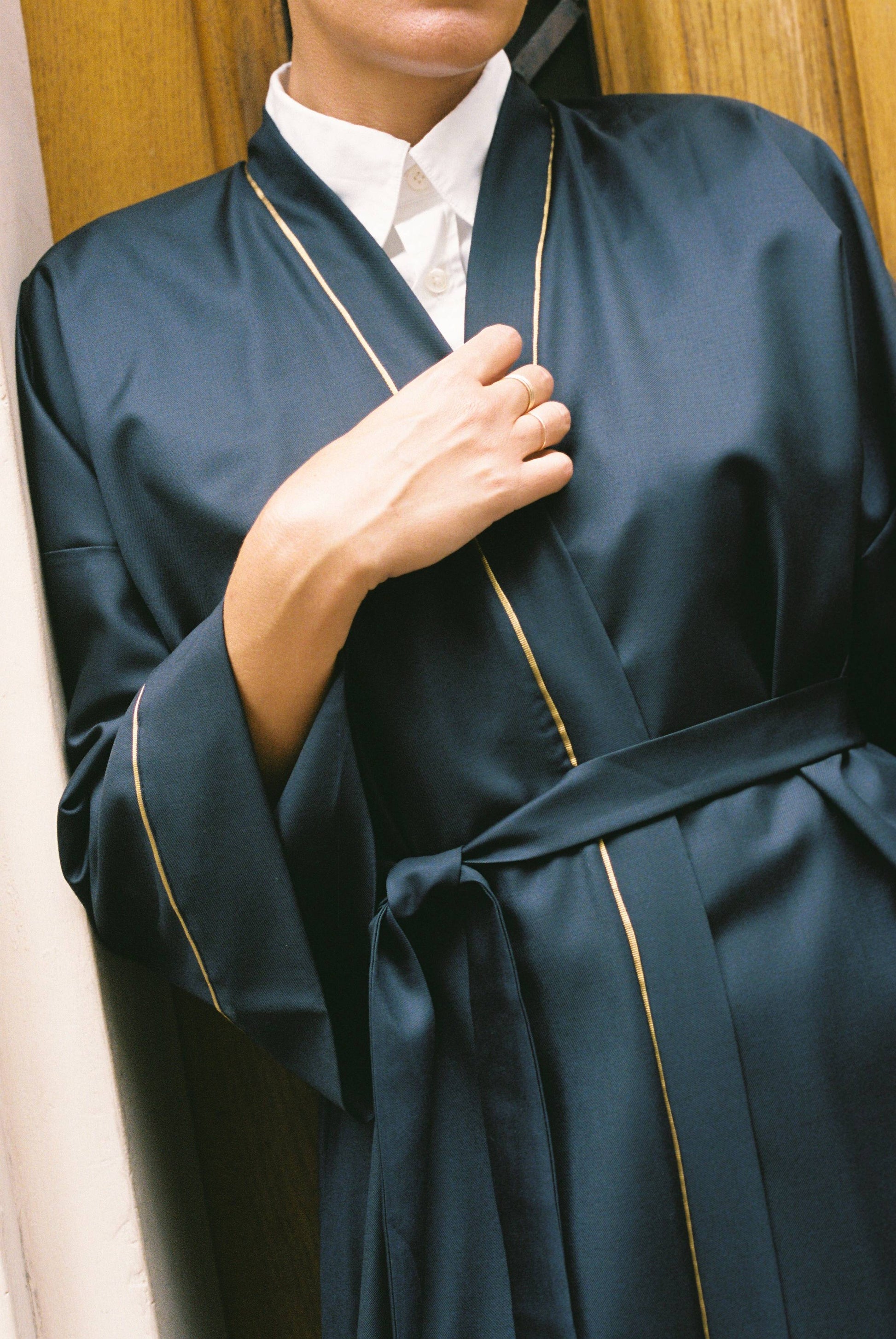 Atelier Sarita – Kimono Garnier en laine de costume bleu marine, rehaussé de délicats passepoils en soie dorée. Une coupe longue et fluide, inspirée de l’élégance intemporelle de l’Opéra Garnier, qui incarne la grandeur et la finesse de l’architecture parisienne. Fabriqué à la main à Paris en série très limitée, ce kimono allie la profondeur classique du bleu marine à la lumière subtile de l’or, pour une silhouette sophistiquée et affirmée.