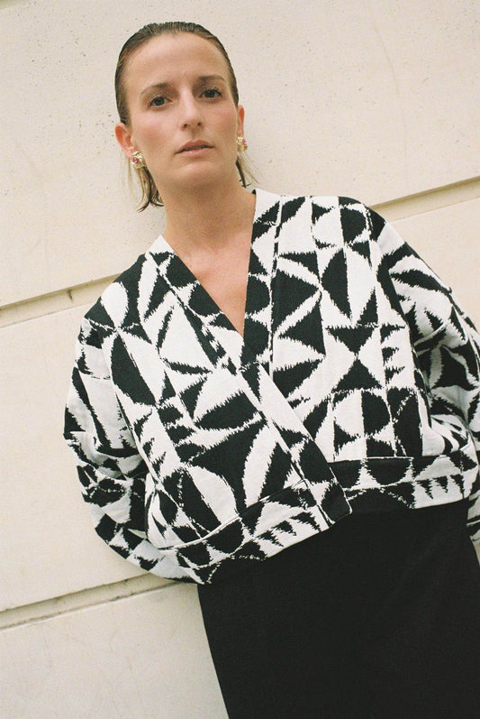 Atelier Sarita – Kimono Kuma en jacquard noir et blanc. Version courte et structurée du kimono, confectionnée à la main à Paris en série limitée. Réalisée dans un jacquard épais mais souple provenant d’une maison de textile française reconnue depuis plus de 200 ans pour son exigence en matière de traçabilité, de production locale et de durabilité. Une pièce audacieuse et graphique, parfaite pour habiller l’automne avec allure.