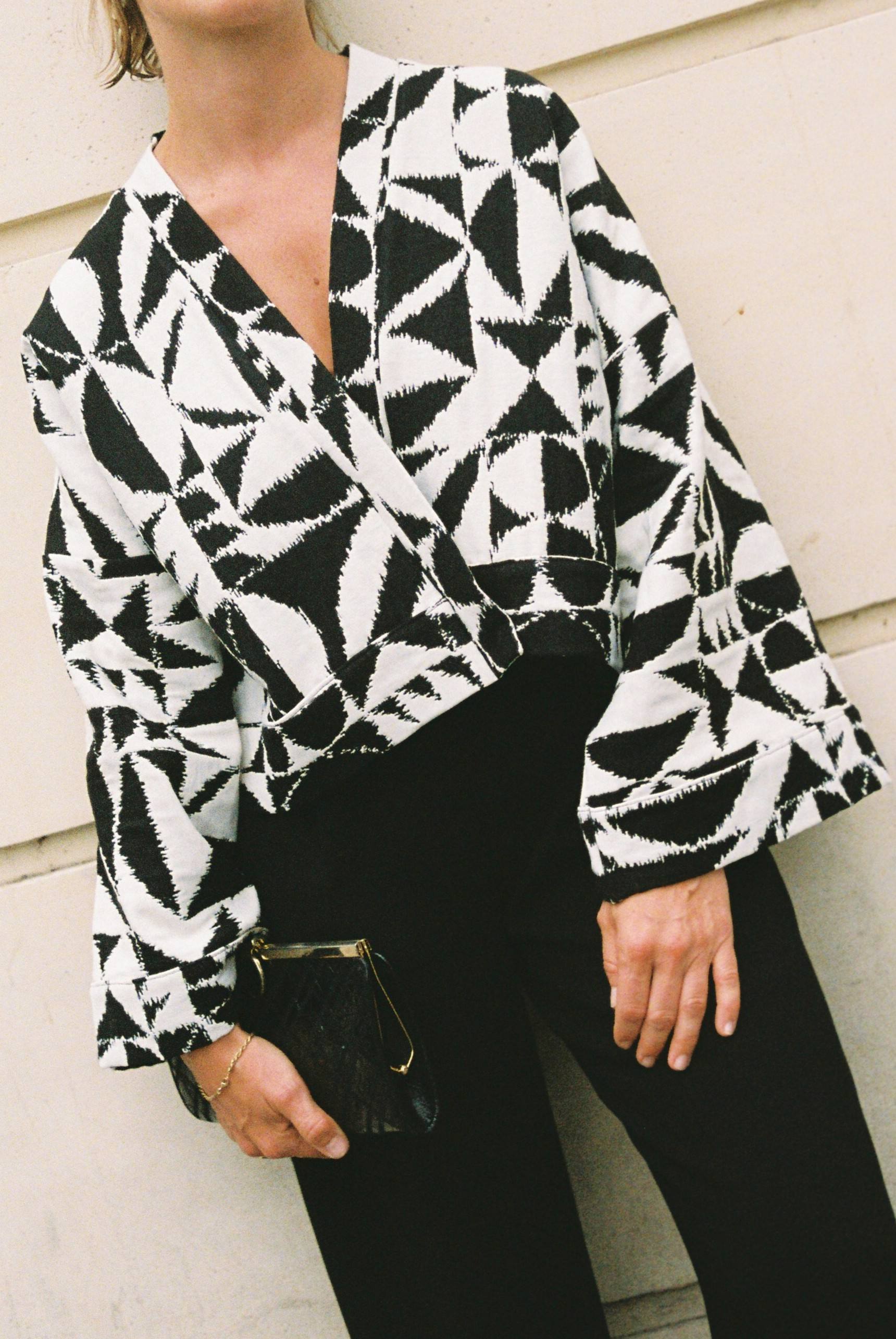 Atelier Sarita – Kimono Kuma en jacquard noir et blanc. Version courte et structurée du kimono, confectionnée à la main à Paris en série limitée. Réalisée dans un jacquard épais mais souple provenant d’une maison de textile française reconnue depuis plus de 200 ans pour son exigence en matière de traçabilité, de production locale et de durabilité. Une pièce audacieuse et graphique, parfaite pour habiller l’automne avec allure.