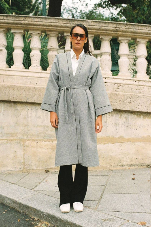 Atelier Sarita – Kimono Mansart en laine de costume pied-de-poule. Long kimono ceinturé à la coupe architecturale, confectionné à la main à Paris en série limitée. Inspiré par la rigueur classique et l’élégance intemporelle, il revisite le tissu tailleur en une pièce urbaine et contemporaine.