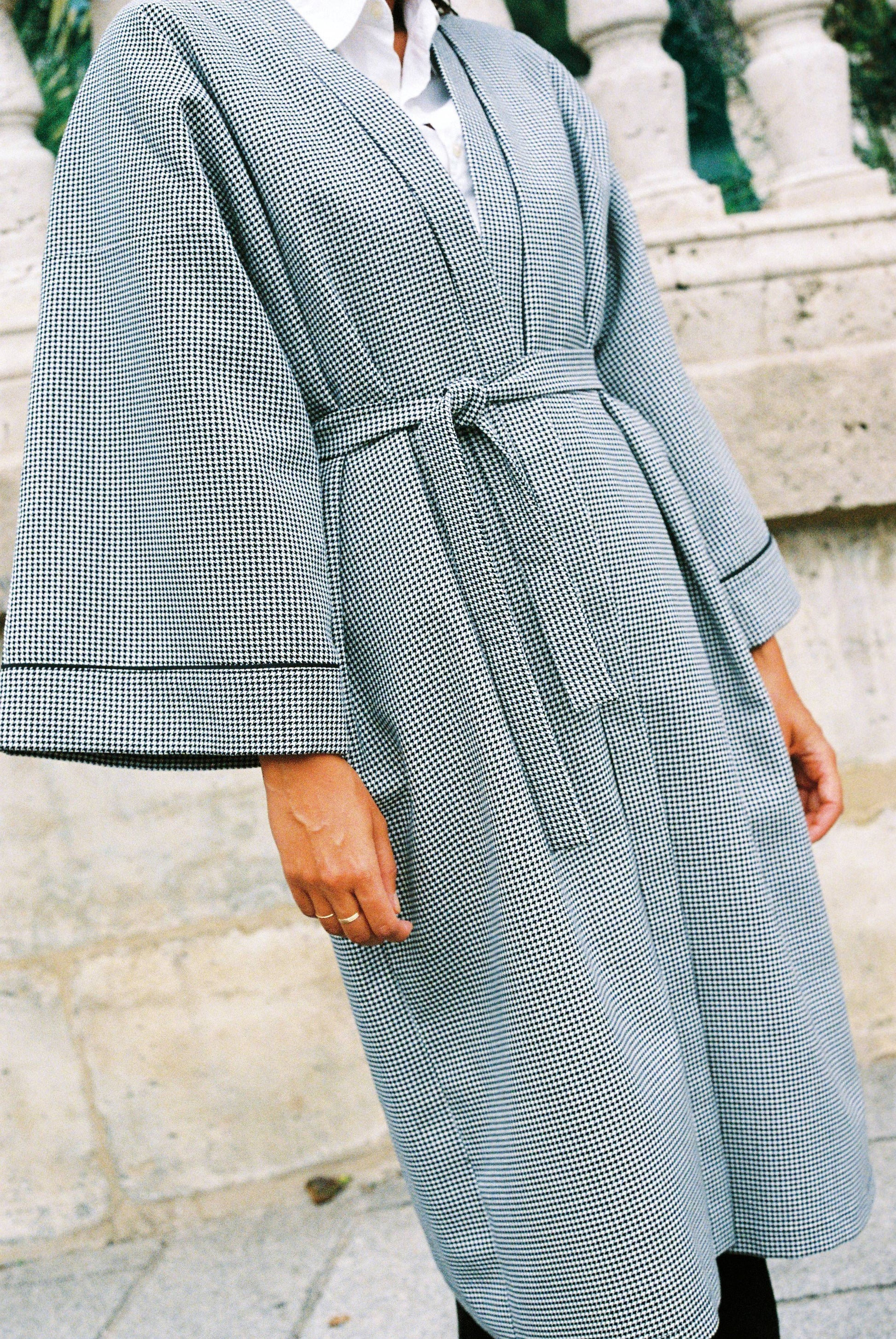 Atelier Sarita – Kimono Mansart en laine de costume pied-de-poule. Long kimono ceinturé à la coupe architecturale, confectionné à la main à Paris en série limitée. Inspiré par la rigueur classique et l’élégance intemporelle, il revisite le tissu tailleur en une pièce urbaine et contemporaine.