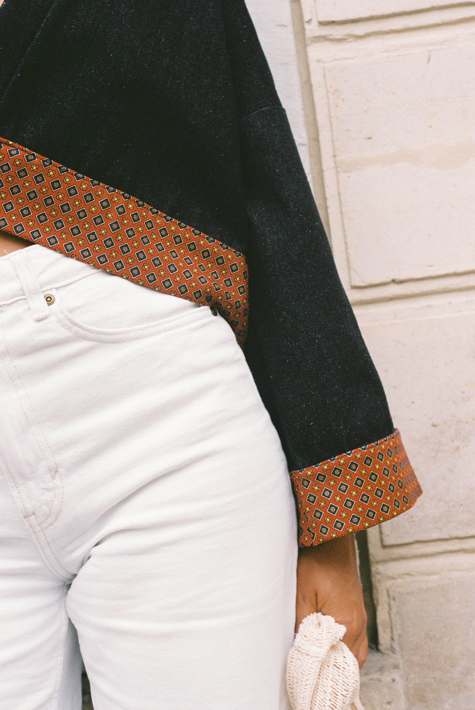 Atelier Sarita – Kimono Perret en denim noir avec parements en soie et laine rouge à motifs géométriques. Veste kimono courte et structurée, confectionnée à la main à Paris à partir de matières naturelles et upcyclées. Une pièce urbaine inspirée de l’architecture parisienne et pensée pour un vestiaire élégant et responsable.