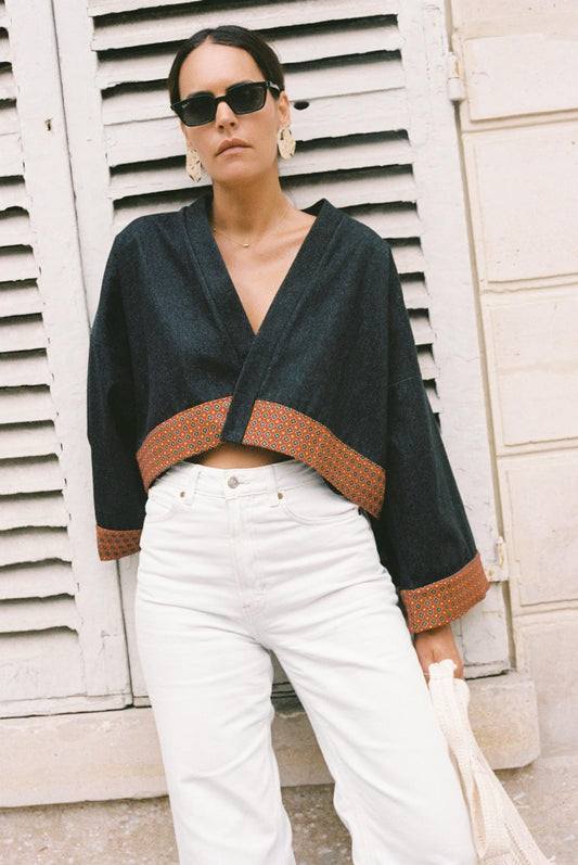 Atelier Sarita – Kimono Perret en denim noir avec parements en soie et laine rouge à motifs géométriques. Veste kimono courte et structurée, confectionnée à la main à Paris à partir de matières naturelles et upcyclées. Une pièce urbaine inspirée de l’architecture parisienne et pensée pour un vestiaire élégant et responsable.