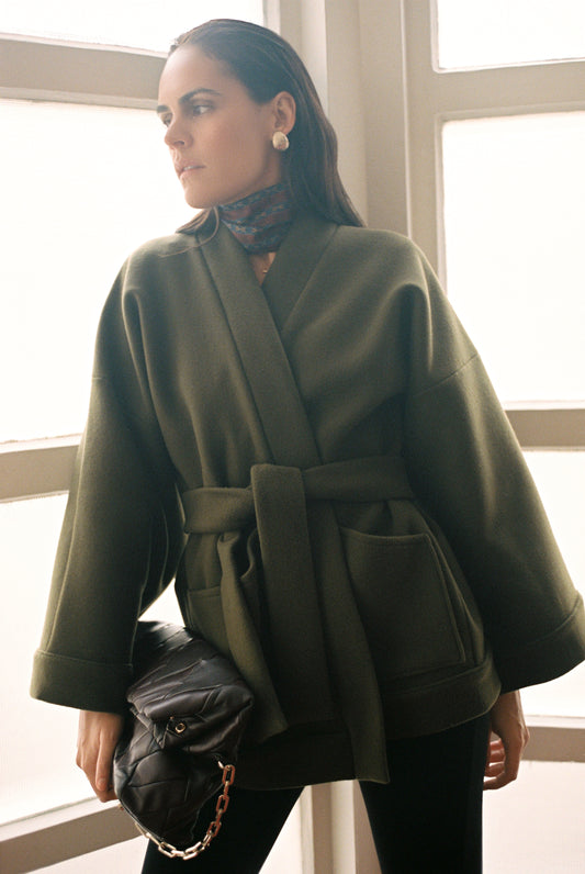 Femme portant le kimono RICHELIEU en laine et cachemire kaki d’Atelier Sarita, coupe veste avec grandes poches plaquées. Kimono structuré, fabriqué à la main à Paris dans un lainage italien issu de stocks dormants de maison de luxe. Modèle chaud, élégant et intemporel, photographié ans un style urbain parisien.