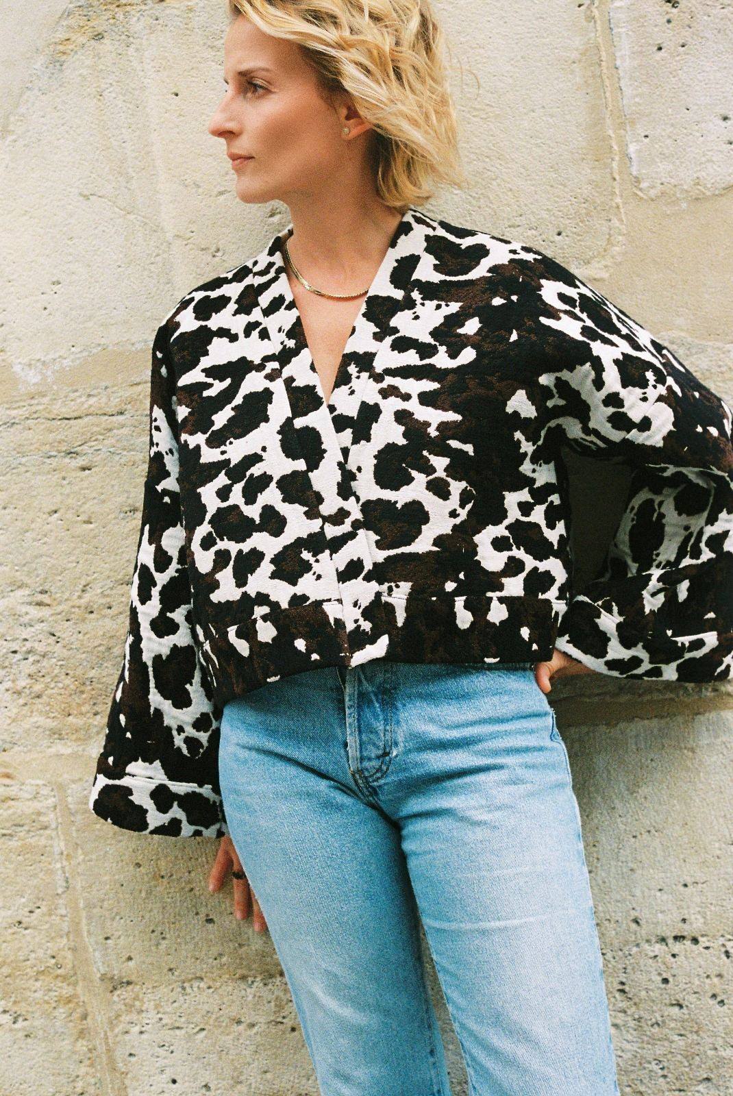 Atelier Sarita – Kimono Roger en jacquard motif vache. Une coupe courte et audacieuse, pensée comme une pièce arty et urbaine, qui bouscule les codes du vestiaire parisien. Confectionné à la main à Paris en série limitée, ce kimono est réalisé dans un jacquard épais et texturé, issu d’une maison textile française reconnue pour son savoir-faire et son exigence en matière de durabilité. Une pièce singulière qui célèbre l’originalité et le mouvement urbain.