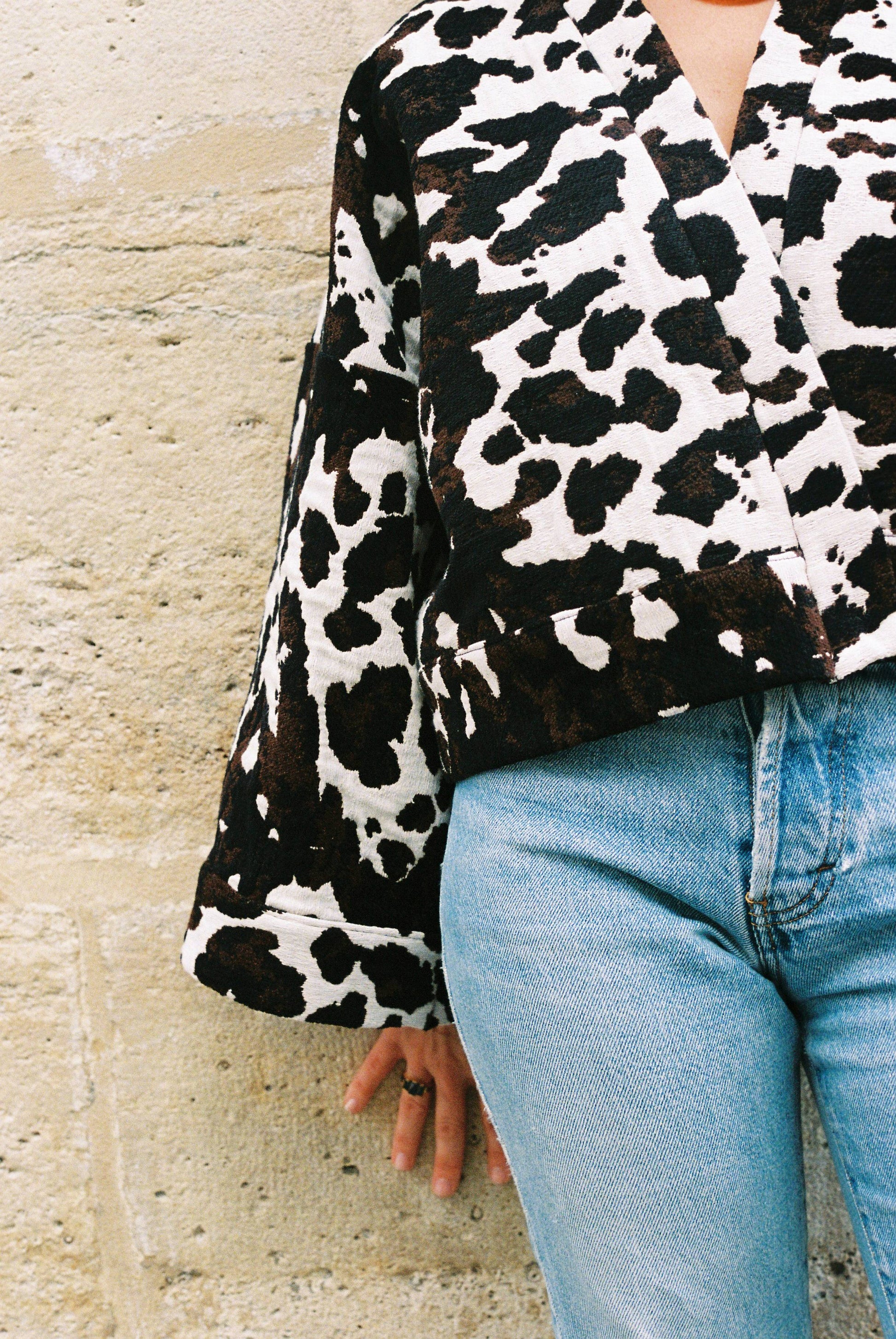 Atelier Sarita – Kimono Roger en jacquard motif vache. Une coupe courte et audacieuse, pensée comme une pièce arty et urbaine, qui bouscule les codes du vestiaire parisien. Confectionné à la main à Paris en série limitée, ce kimono est réalisé dans un jacquard épais et texturé, issu d’une maison textile française reconnue pour son savoir-faire et son exigence en matière de durabilité. Une pièce singulière qui célèbre l’originalité et le mouvement urbain.