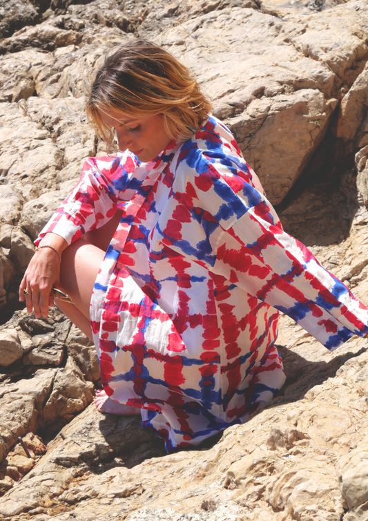 Femme portant un kimono mi-long bleu et fuchsia Atelier Sarita, en voile de coton léger, sur un rocher face à la mer.