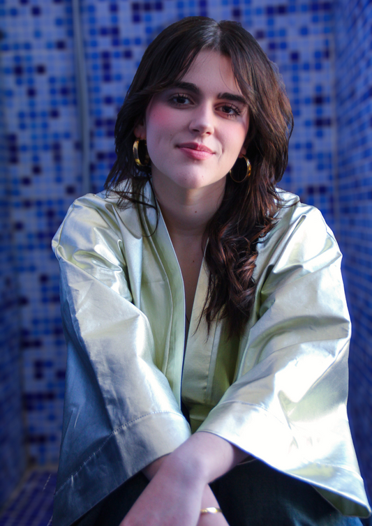 Femme portant un kimono court en coton doré métallisé, photographiée dans une salle de bain aux carreaux bleus.