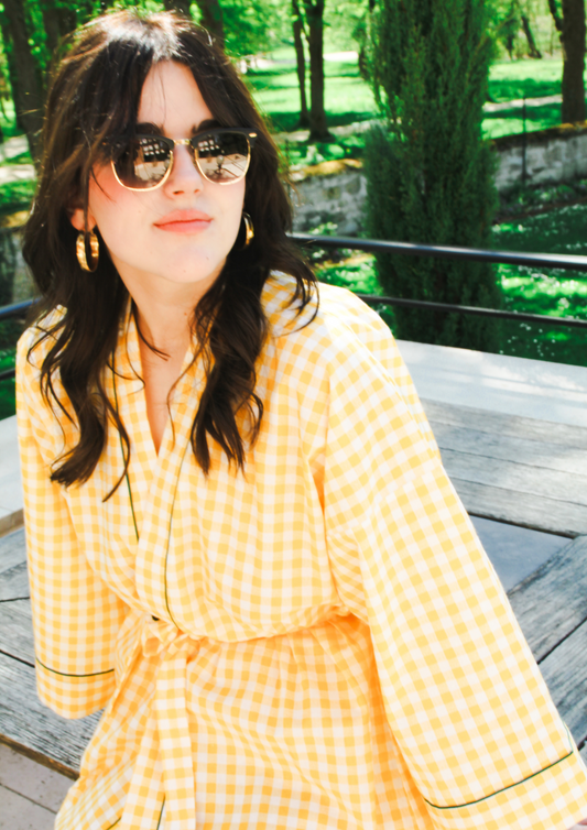 Femme portant un kimono court en coton vichy jaune à passepoil vert, noué à la taille, dans une pièce lumineuse.