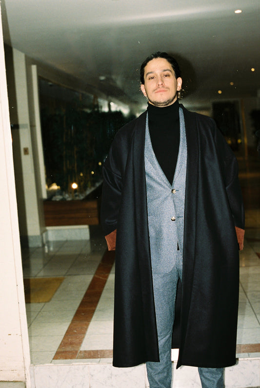 Homme portant le kimono long COLBERT Atelier Sarita en laine caviar noire avec finitions en velours coton couleur oud. Modèle ample et architectural, confectionné à la main à Paris, pensé comme un manteau kimono hivernal unisexe.