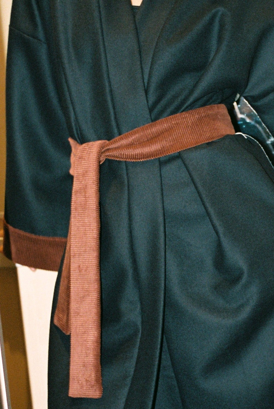Personne portant le kimono long COLBERT Atelier Sarita en laine caviar noire avec finitions en velours coton couleur oud. Modèle ample et architectural, confectionné à la main à Paris, pensé comme un manteau kimono hivernal unisexe.