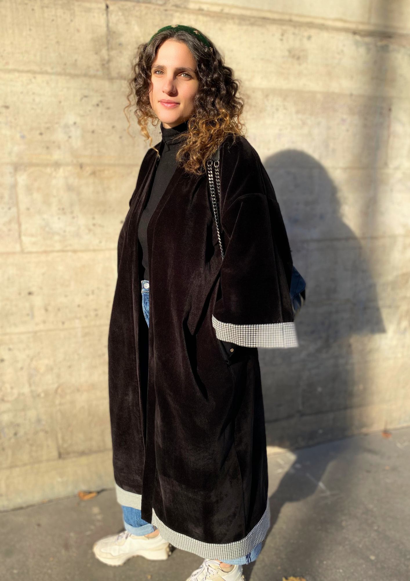 Jeune femme vêtue d'un Kimono long en velours noir avec détails laine vichy aux poignets et à l'ourlet, coupe fluide et manches larges, porté ouvert.