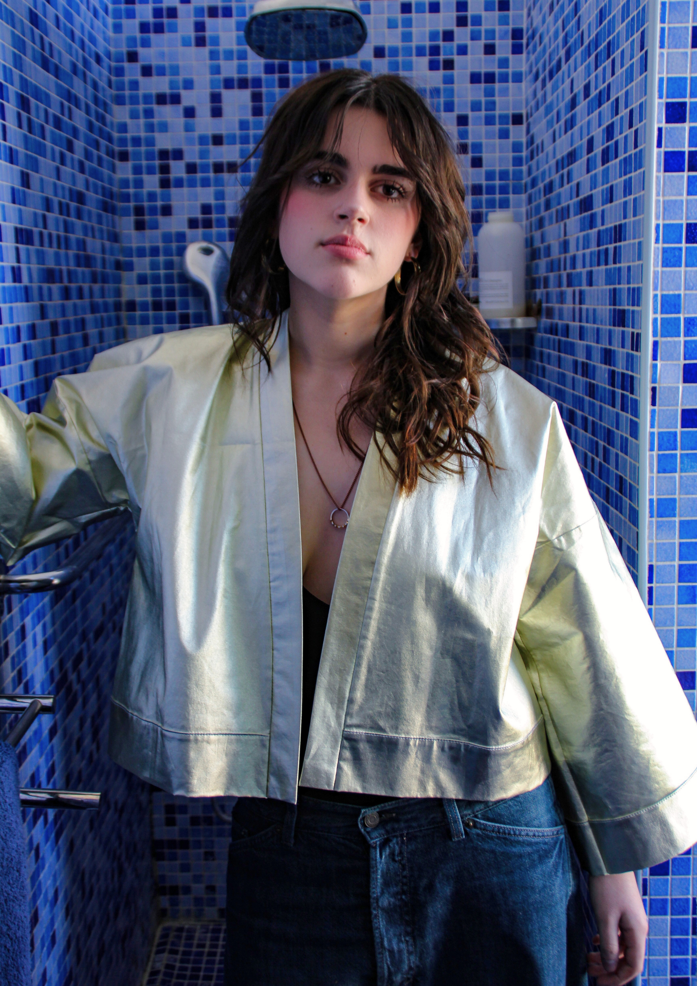 Femme portant un kimono court en coton doré métallisé, photographiée dans une salle de bain aux carreaux bleus.