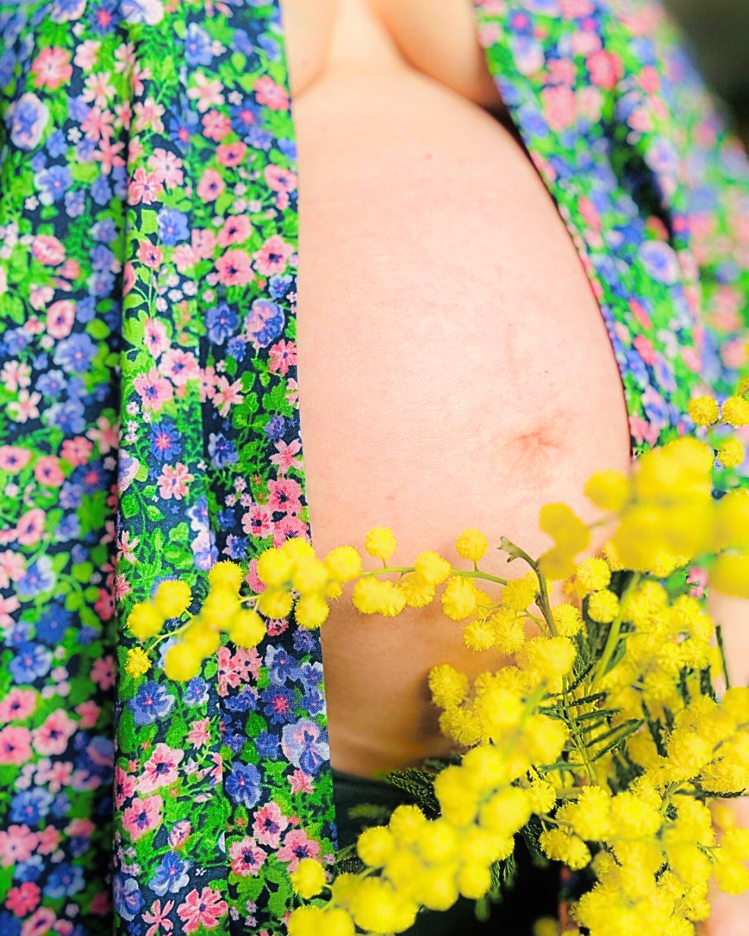 Douceur et féminité : maternité sublimée par la nature.
Gros plan sur un ventre de femme enceinte, entouré d’un kimono à motifs fleuris et de branches de mimosa jaune, évoquant la douceur, la féminité et la connexion avec la nature.