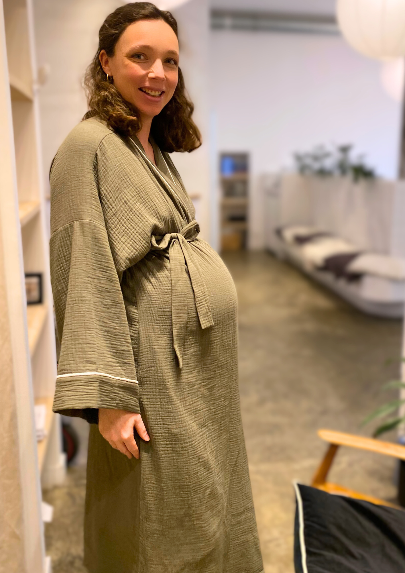 Jeune femme enceinte vêtue d'un Kimono de maternité en gaze de coton kaki avec liseré blanc, coupe ample et enveloppante pour un confort optimal.
