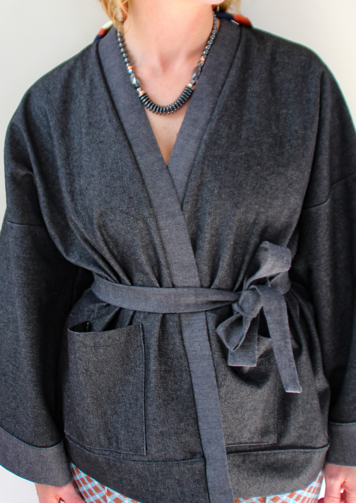 Femme portant un kimono court en denim noir 100% coton, avec manches larges et poches plaquées, fait à la main à Paris.