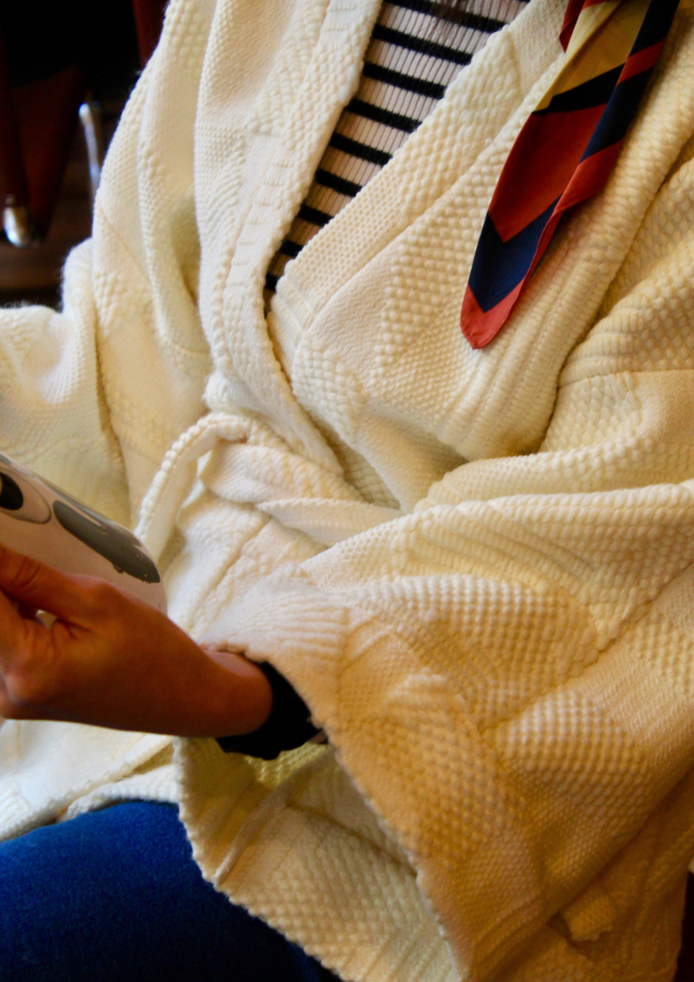 Jeune femme au look retro porte un kimono en laine blanc cassé, doux et élégant, idéal pour les douces journées printanières. Cette pièce unique est confectionnée à la main avec soin à Paris.