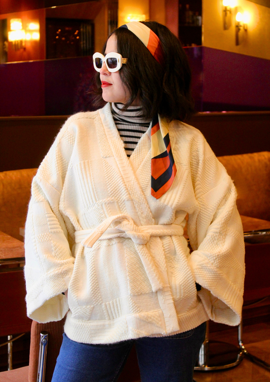 Jeune femme au look retro porte un kimono en laine blanc cassé, doux et élégant, idéal pour les douces journées printanières. Cette pièce unique est confectionnée à la main avec soin à Paris.