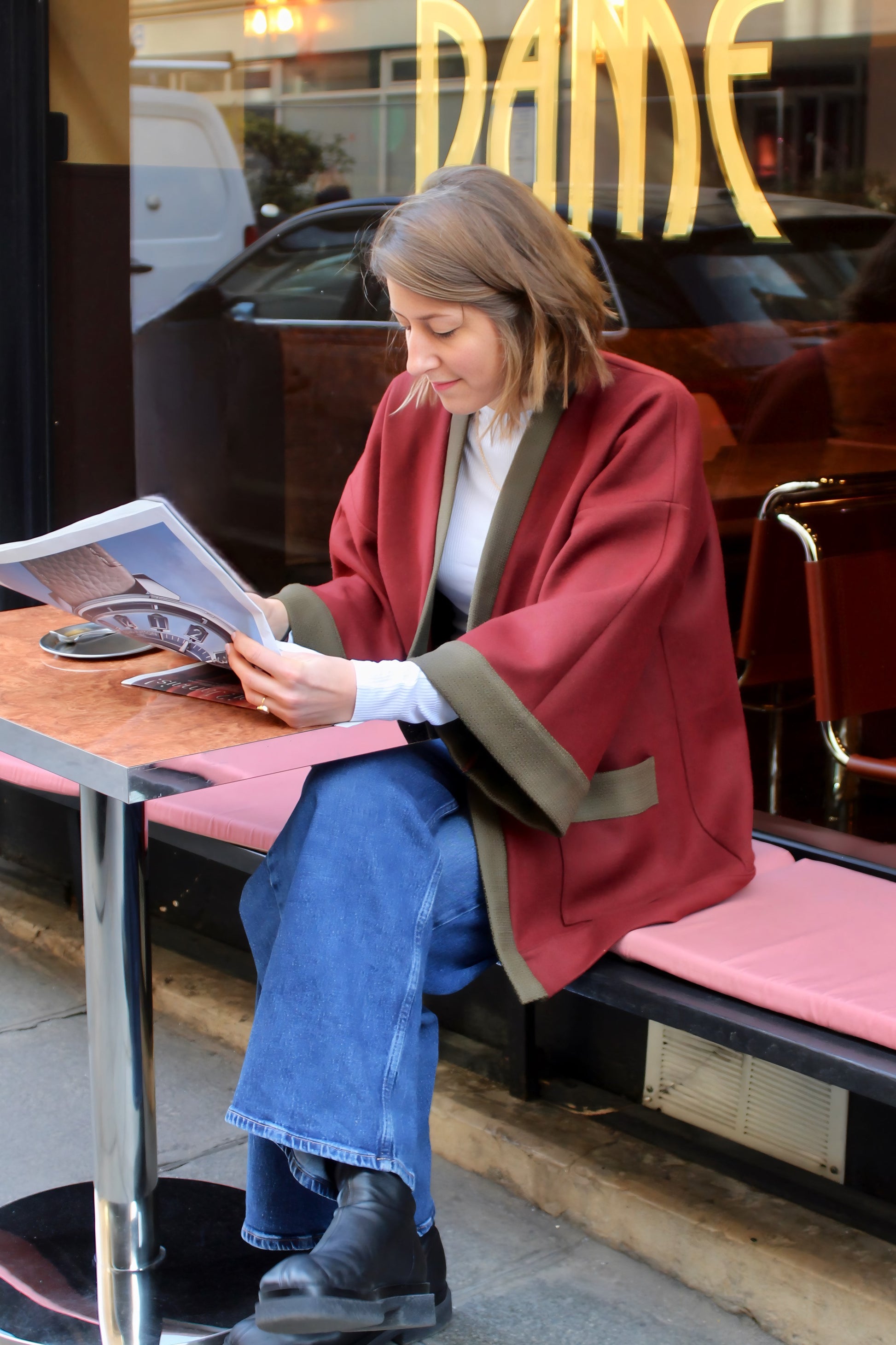 Jeune femme à la terrasse d'un café, lisant le journal en kimono en laine bordeaux et kaki.