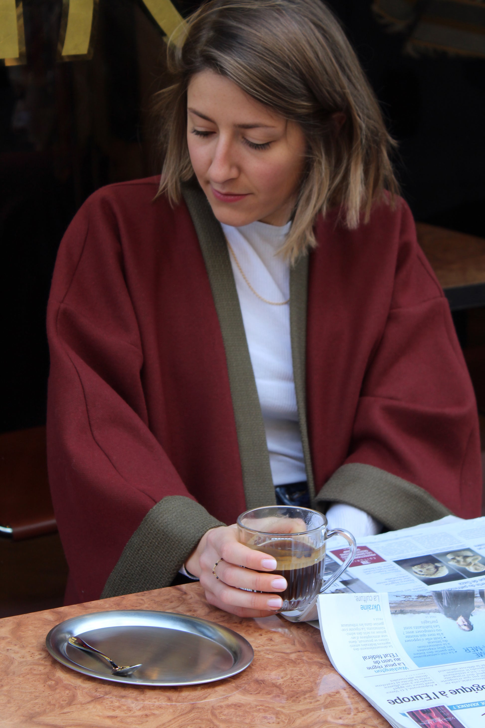 Jeune femme à la terrasse d'un café, lisant le journal en kimono en laine bordeaux et kaki.