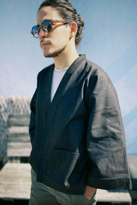 Homme portant un kimono court en denim noir 100% coton, avec manches larges et poches plaquées, fait à la main à Paris.