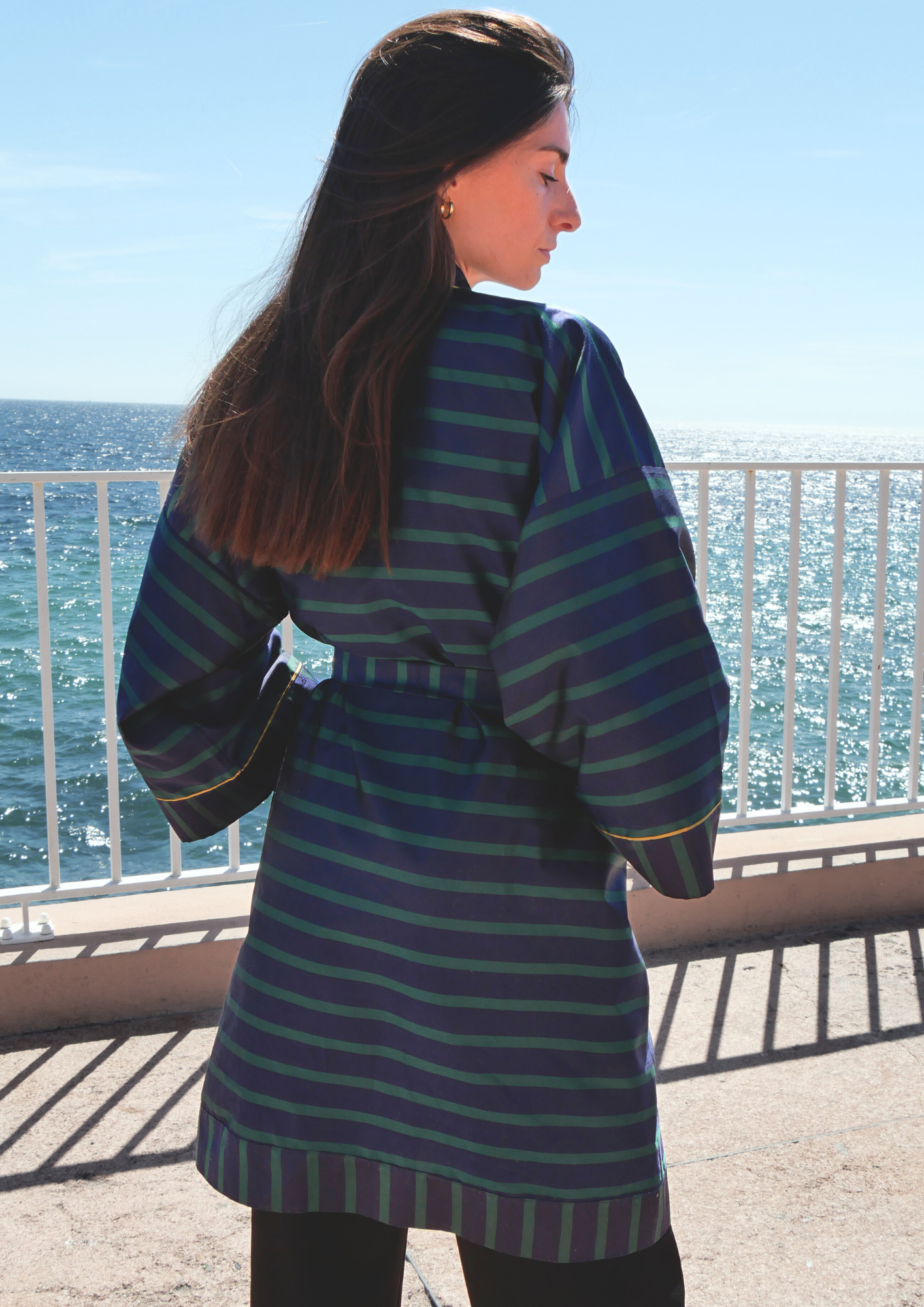 Femme portant un kimono mi-long en soie bleu et vert rehaussé d’un liseré doré, modèle Atelier Sarita fait main à Paris.