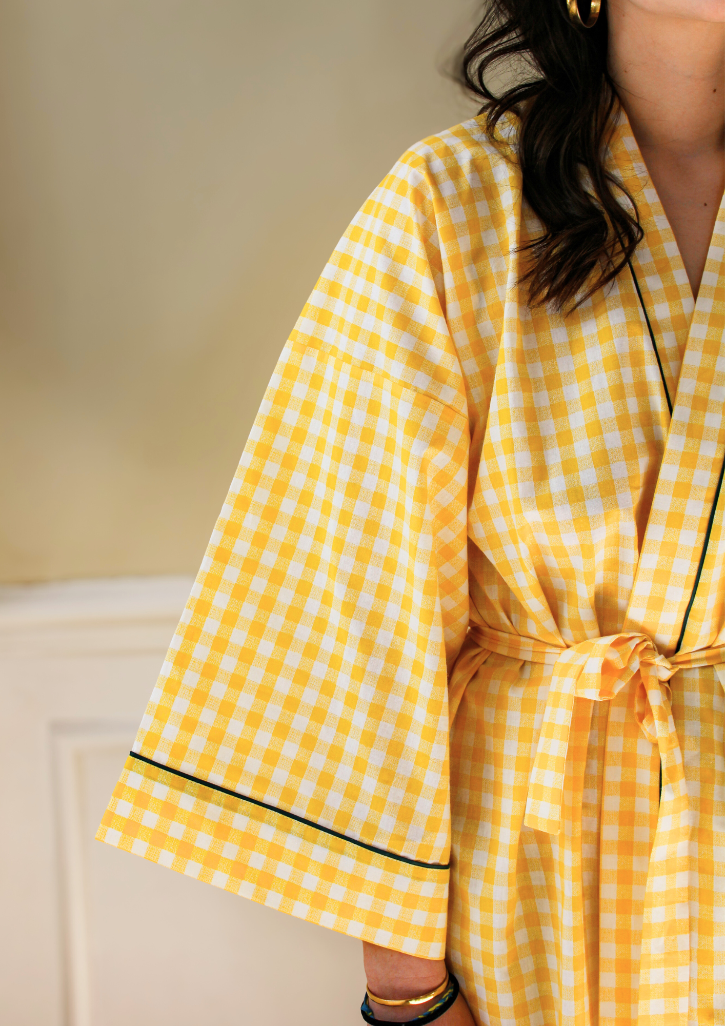 Femme portant un kimono court en coton vichy jaune à passepoil vert, noué à la taille, dans une pièce lumineuse.