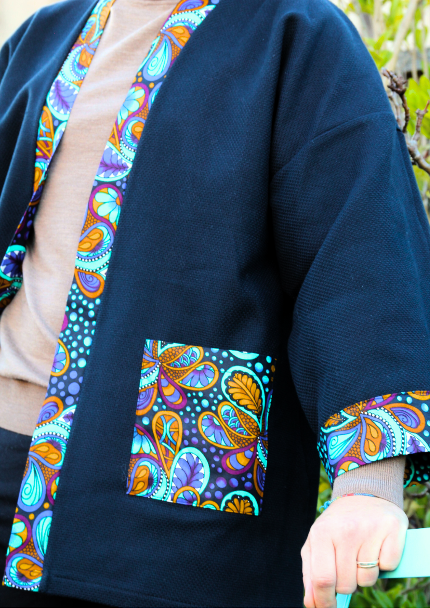 Homme portant un kimono court en coton bleu avec finitions en wax coloré, manches larges et poches assorties.