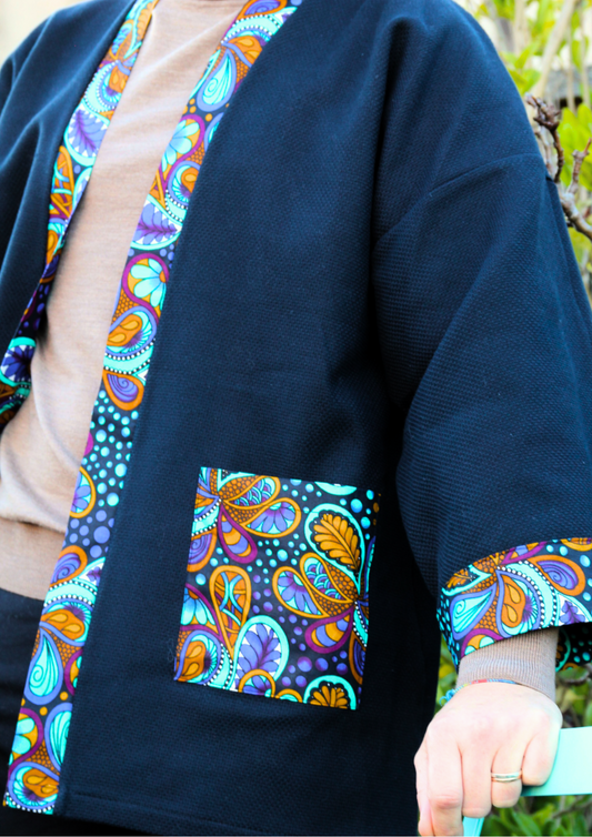 Homme portant un kimono court en coton bleu avec finitions en wax coloré, manches larges et poches assorties.