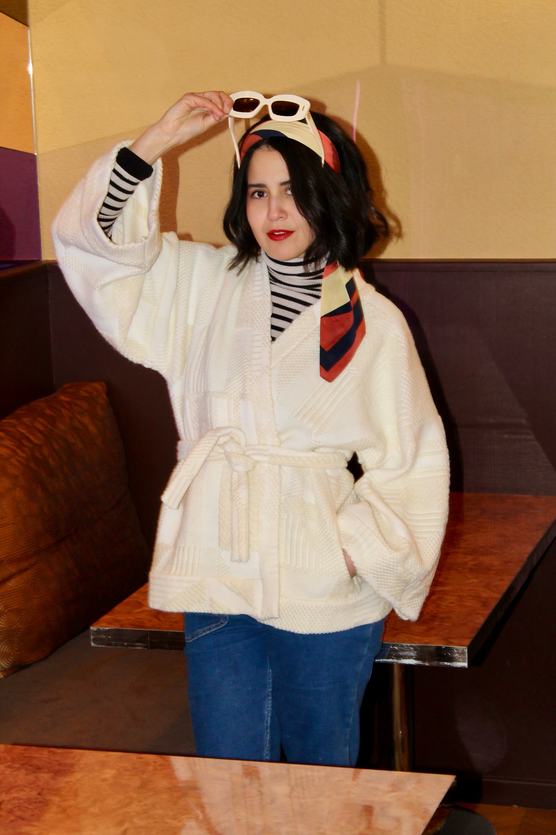 Jeune femme au look retro porte un kimono en laine blanc cassé, doux et élégant, idéal pour les douces journées printanières. Cette pièce unique est confectionnée à la main avec soin à Paris.