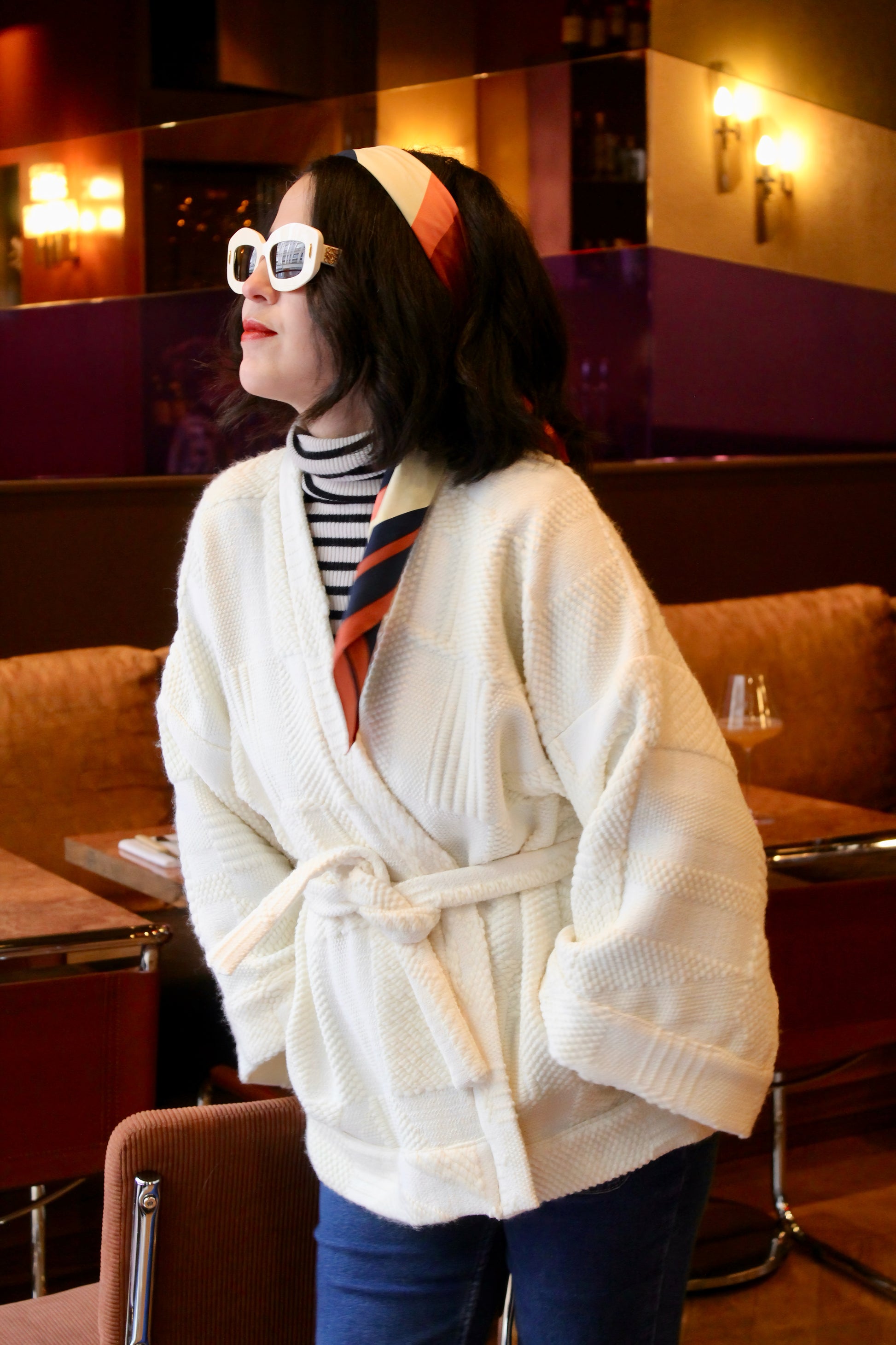 Jeune femme au look retro porte un kimono en laine blanc cassé, doux et élégant, idéal pour les douces journées printanières. Cette pièce unique est confectionnée à la main avec soin à Paris.