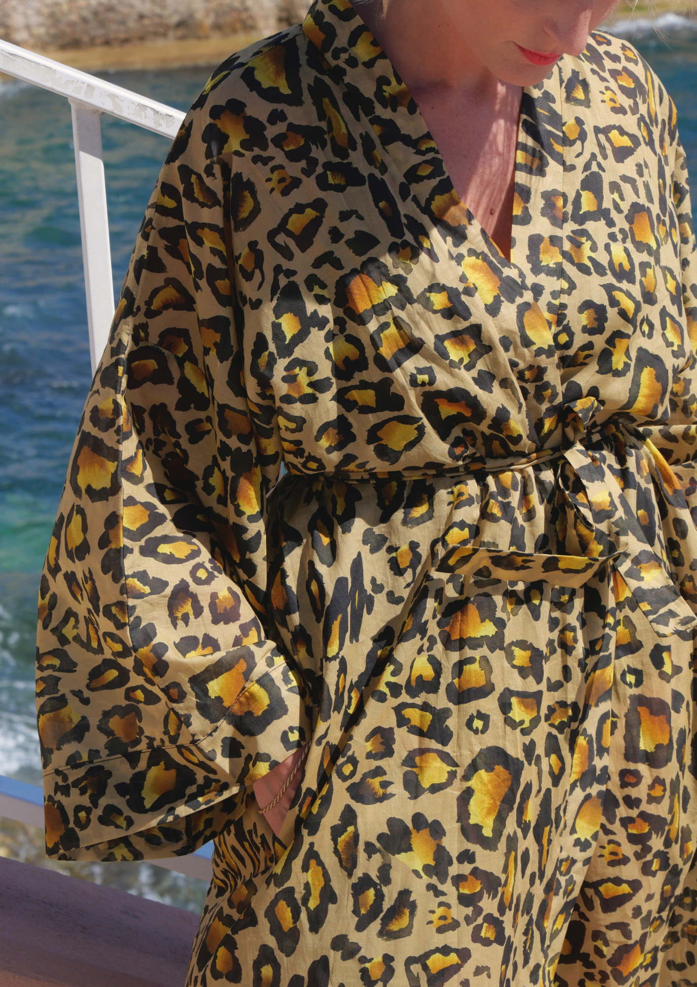 Femme portant un kimono long en voile de coton à imprimé léopard, ceinturé à la taille, posant face à la mer sous le soleil – création Atelier Sarita, confectionnée à la main à Paris.