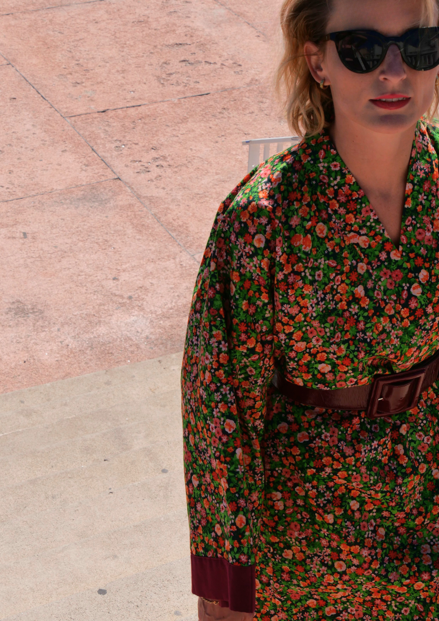 Femme portant un kimono long fleuri en coton avec finitions bordeaux, ceinturé à la taille, debout sur une terrasse ensoleillée – création Atelier Sarita, confectionnée à la main à Paris.