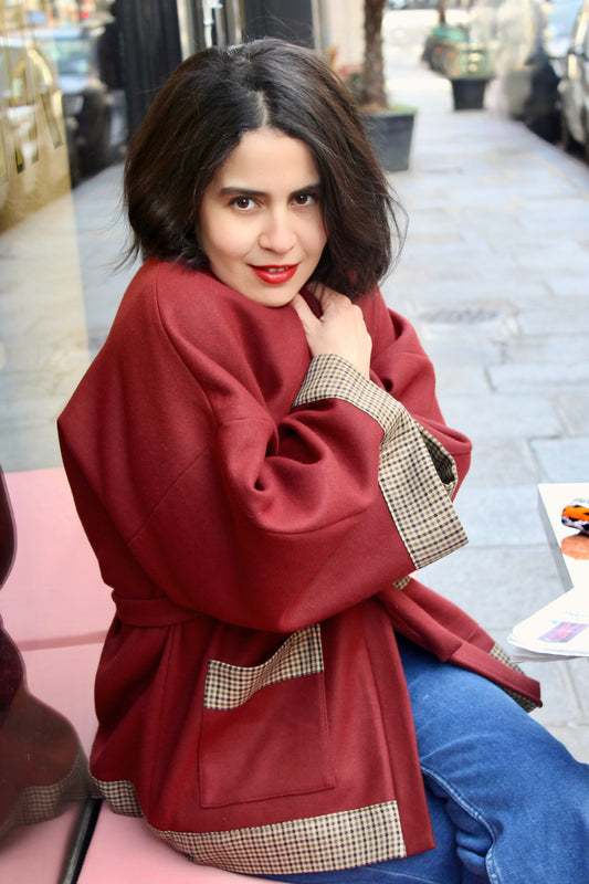 Jeune femme à la terrasse d'un café parisien, portant un kimono en laine bordeaux et finitions en laine pied de poule.