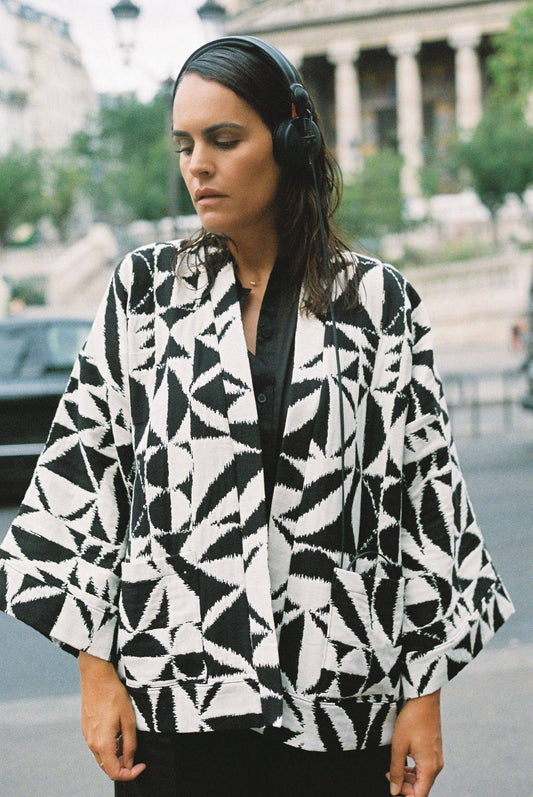 Atelier Sarita – Kimono Ito en jacquard noir et blanc. Une coupe ample et enveloppante, pensée pour épouser le mouvement urbain avec assurance et élégance. Confectionné à la main à Paris en série limitée, ce modèle est réalisé dans un jacquard graphique épais mais souple, provenant d’une maison de textile française fondée il y a plus de 200 ans et reconnue pour son exigence en matière de traçabilité, de production locale et de durabilité. Une pièce forte et audacieuse, parfaite pour l’automne.