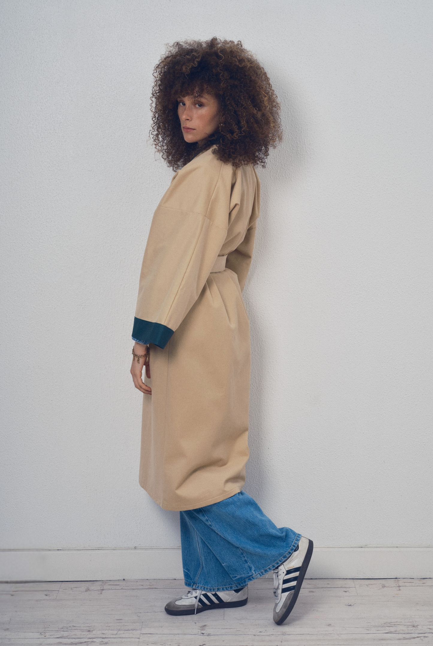 Trench beige aux lignes kimono avec finitions vert foncé porté ceinturé, modèle Charlot de la collection Côté Marais par Atelier Sarita.