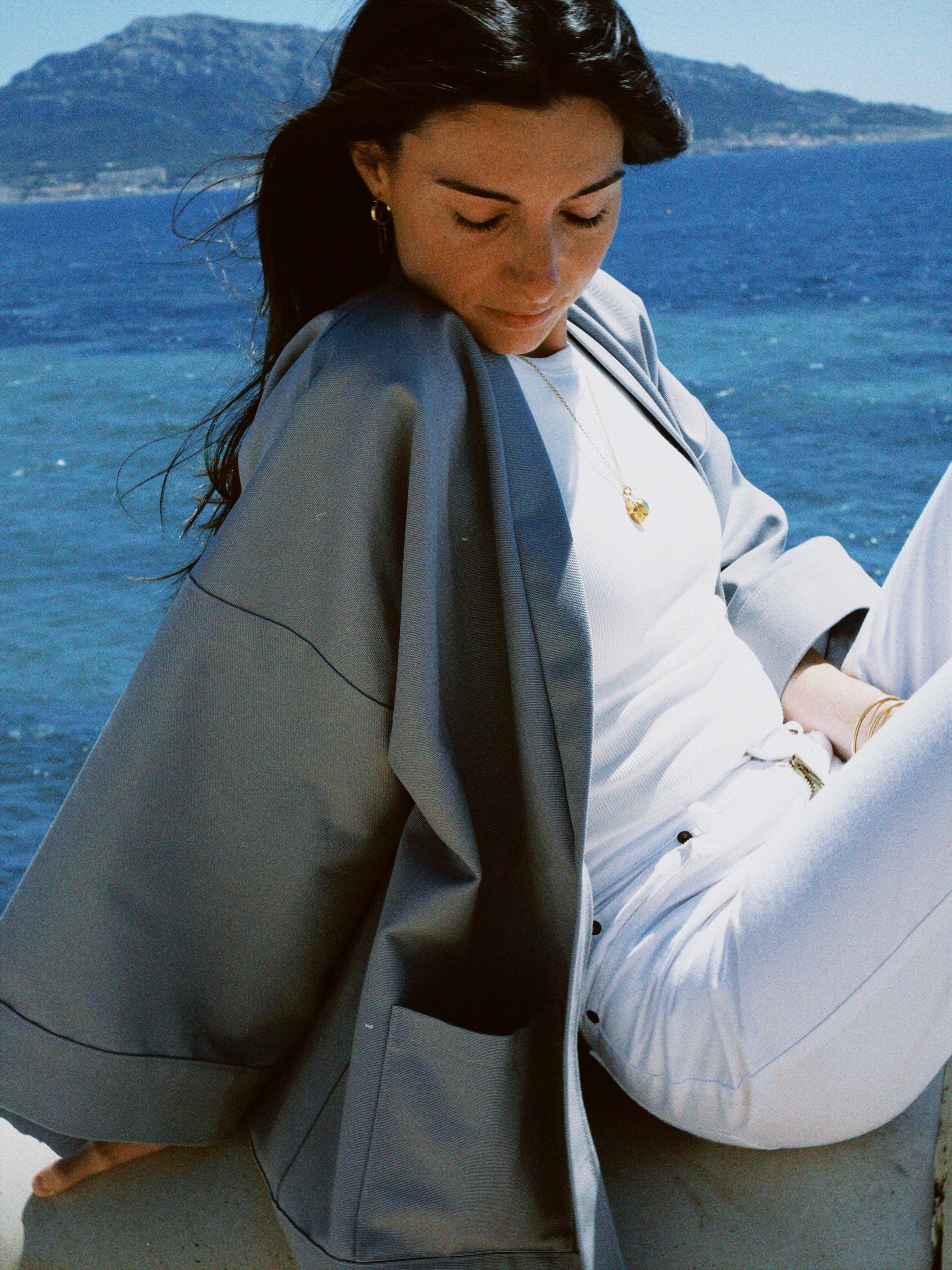 Femme portant un kimono gris en coton biologique, coupe ample avec ceinture, photographiée en bord de mer. Pièce confectionnée à la main à Paris, par Atelier Sarita.