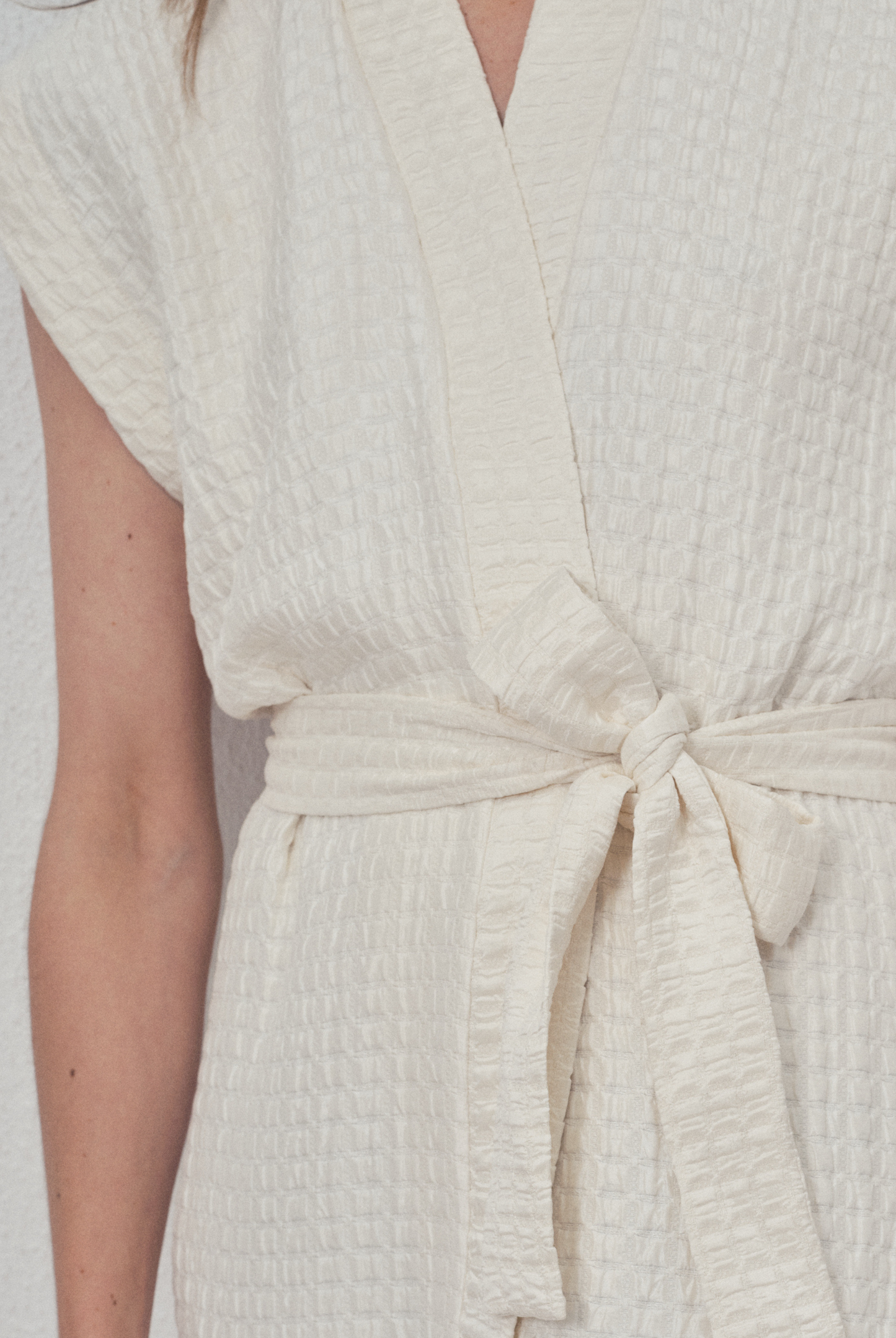 Robe portefeuille blanche en soie texturée portée avec des bottines noires et un perfecto en cuir noir, modèle Pastourelle de la collection Côté Marais par Atelier Sarita.