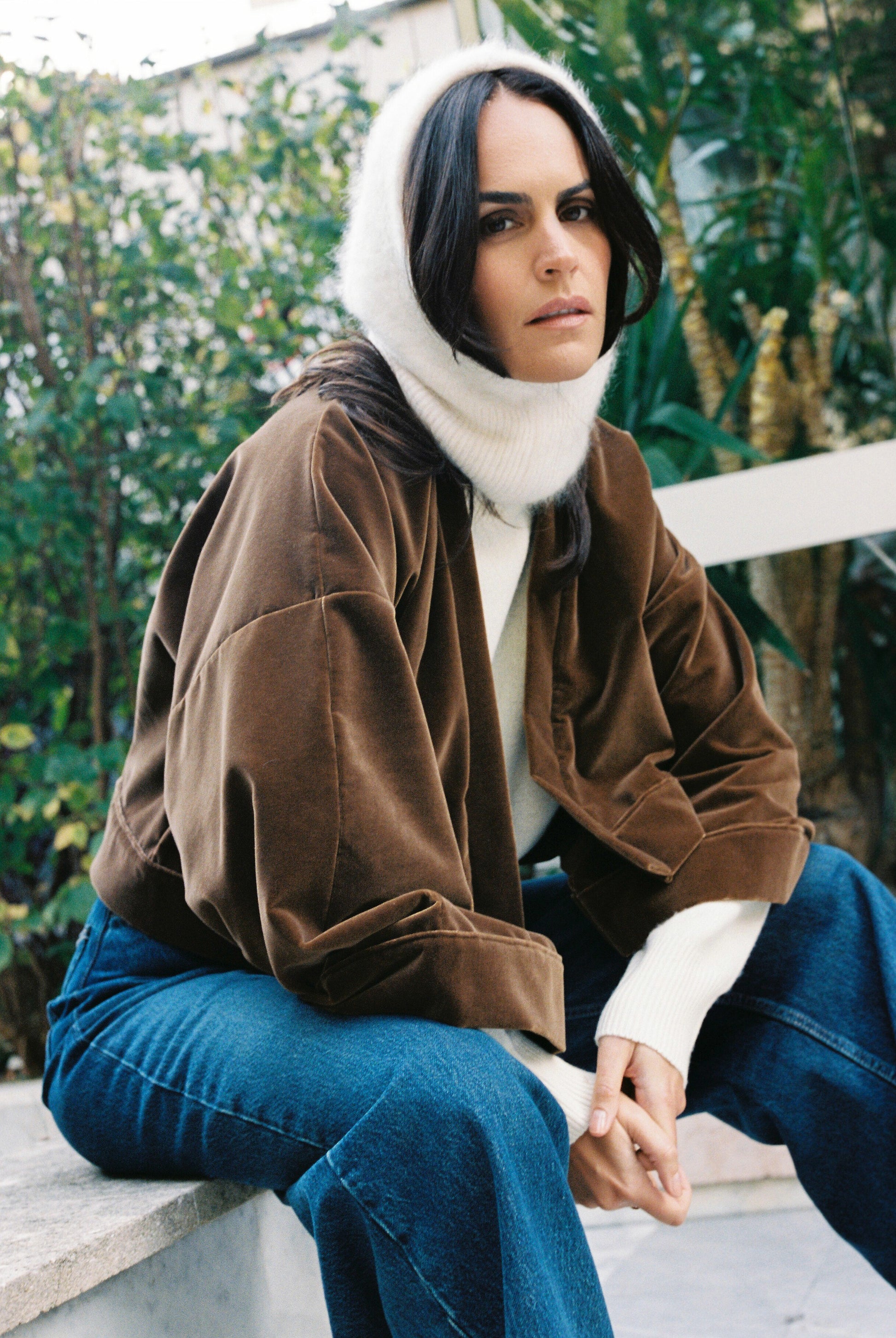 Femme portant le kimono court BRADY en velours de coton marron café Atelier Sarita avec poches intégrées. Kimono fabriqué à la main à Paris dans un velours 100 % coton issu de deadstocks. Pièce chaude et texturée, au tombé souple, photographiée en extérieur avec un look hivernal composé d’un pull écru et d’un jean, mettant en valeur la douceur et la profondeur du velours marron.