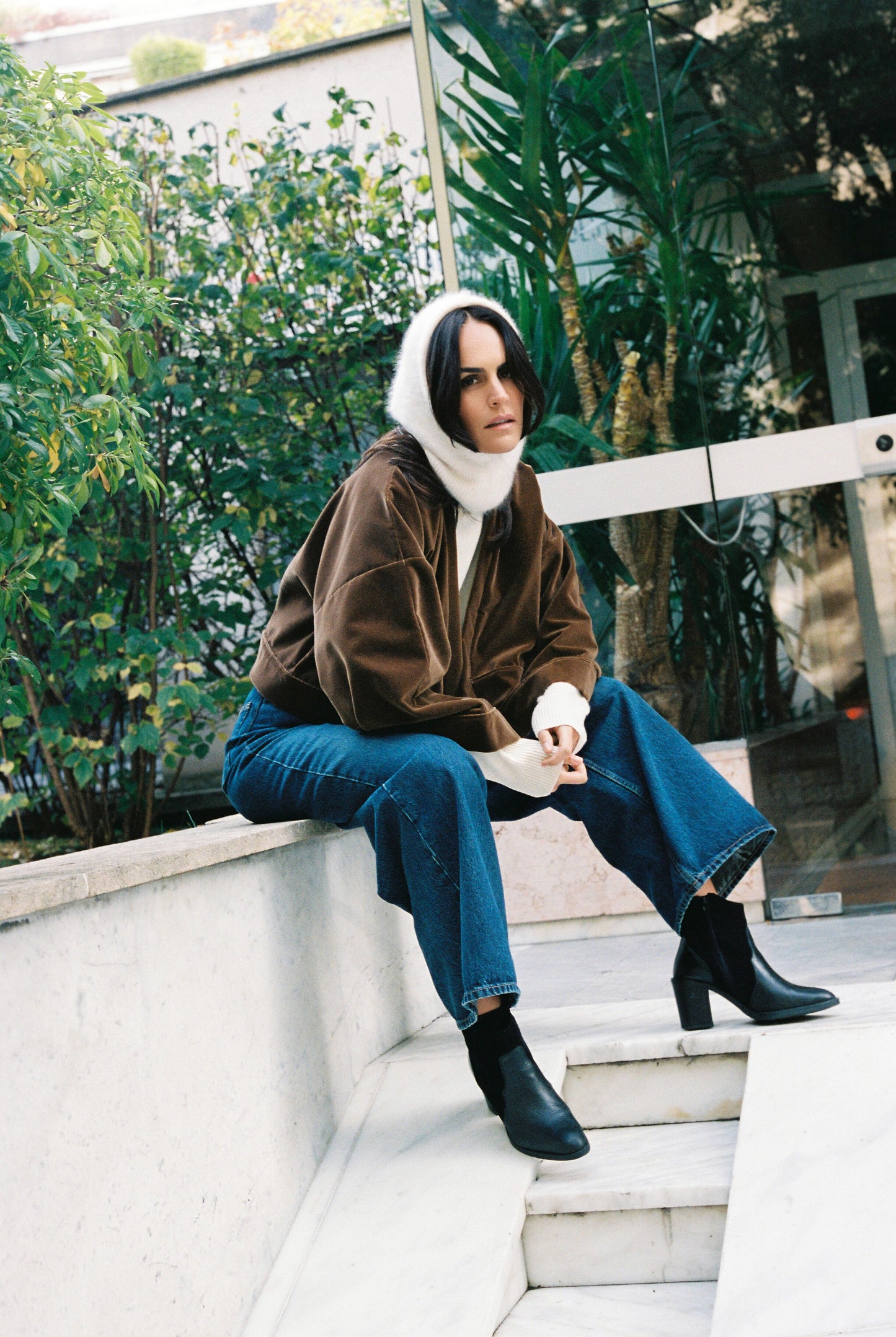 Femme portant le kimono court BRADY en velours de coton marron café Atelier Sarita avec poches intégrées. Kimono fabriqué à la main à Paris dans un velours 100 % coton issu de deadstocks. Pièce chaude et texturée, au tombé souple, photographiée en extérieur avec un look hivernal composé d’un pull écru et d’un jean, mettant en valeur la douceur et la profondeur du velours marron.