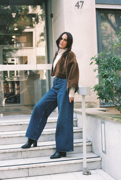 Femme portant le kimono court BRADY en velours de coton marron café Atelier Sarita avec poches intégrées. Kimono fabriqué à la main à Paris dans un velours 100 % coton issu de deadstocks. Pièce chaude et texturée, au tombé souple, photographiée en extérieur avec un look hivernal composé d’un pull écru et d’un jean, mettant en valeur la douceur et la profondeur du velours marron.