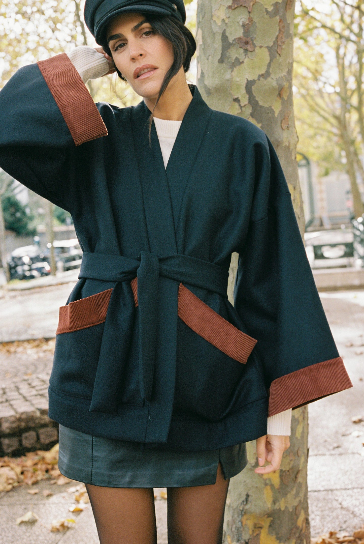 Femme portant le kimono DODAT Atelier Sarita, un kimono veste en laine caviar noire avec finitions en velours coton couleur oud, photographié en extérieur au soleil. Modèle unisexe, confectionné à la main à Paris, au style urbain et architectural.