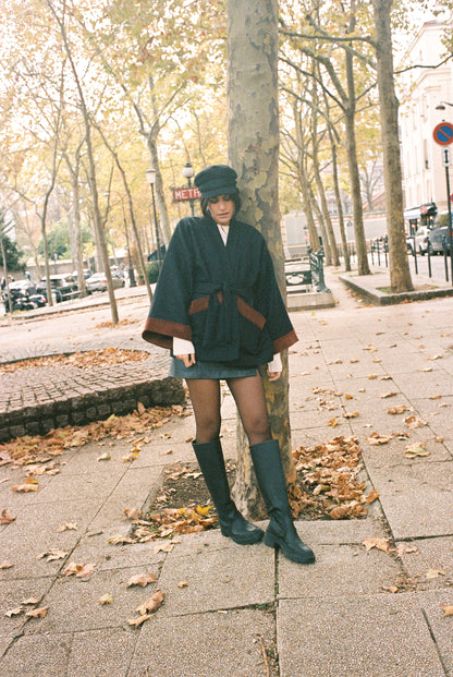 Femme portant le kimono DODAT Atelier Sarita, un kimono veste en laine caviar noire avec finitions en velours coton couleur oud, photographié en extérieur au soleil. Modèle unisexe, confectionné à la main à Paris, au style urbain et architectural.