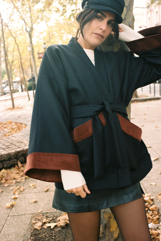 Femme portant le kimono DODAT Atelier Sarita, un kimono veste en laine caviar noire avec finitions en velours coton couleur oud, photographié en extérieur au soleil. Modèle unisexe, confectionné à la main à Paris, au style urbain et architectural.