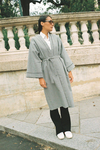 Atelier Sarita – Kimono Mansart en laine de costume pied-de-poule. Long kimono ceinturé à la coupe architecturale, confectionné à la main à Paris en série limitée. Inspiré par la rigueur classique et l’élégance intemporelle, il revisite le tissu tailleur en une pièce urbaine et contemporaine.